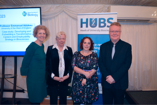 Heads of University Biosciences panel and Dr Kat Arney standing side by side in front of HUBS banner